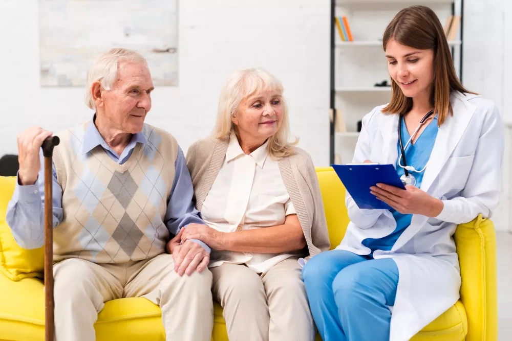 Nurse with blue paper sheet in hands sitting with old couple on a yellow sofa