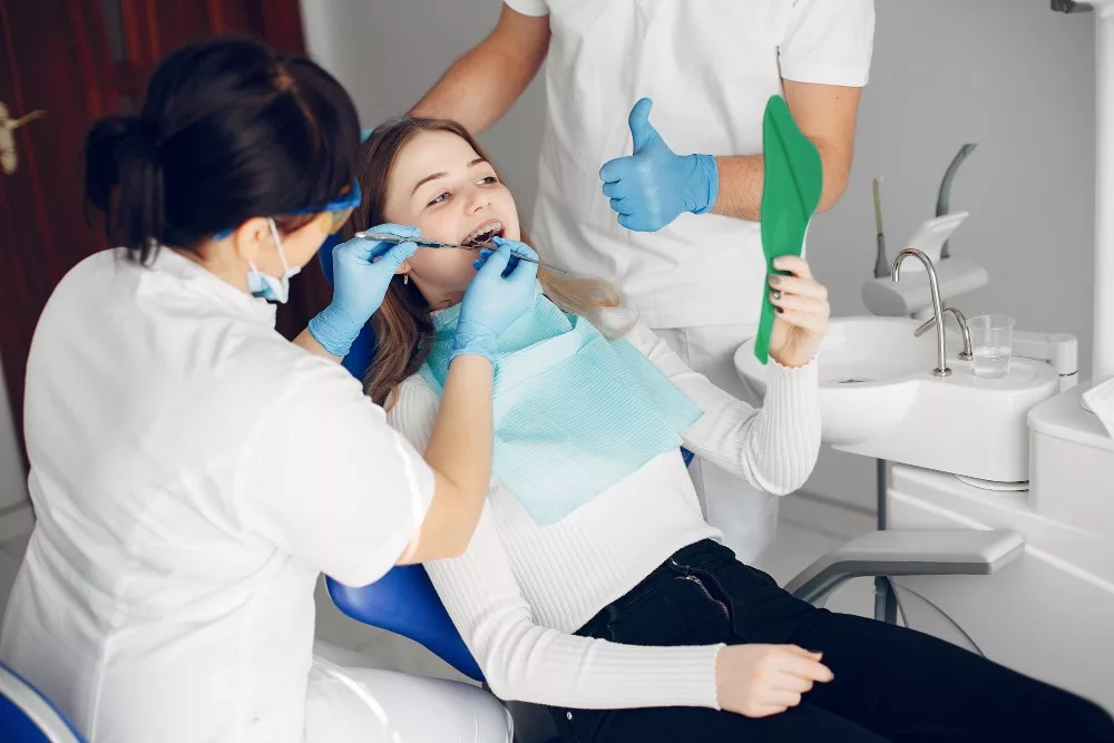 Lady dentist examining a female patient with tools with her assistant